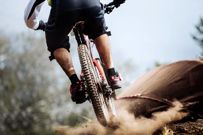 closeup of rear wheel of bike extreme racer on track downhill, dust from wheels