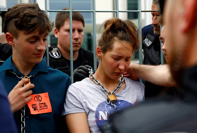 Policisti snemajo verigo okoli vratu podnebnih aktivistov, ki so se protestno priklenili za ograjo pred vlado v Berlinu. FOTO: Fabrizio Bensch/REUTERS