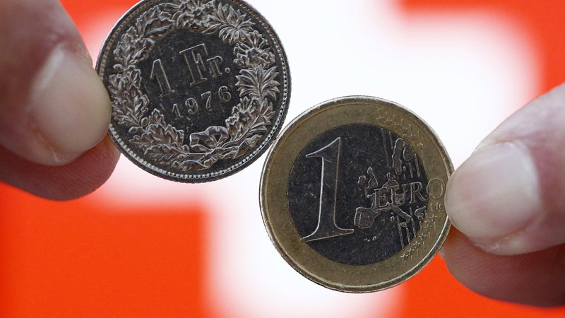 Fotografija: A one Swiss franc coin (L) and a one Euro coin are seen in front of a Swiss flag in this illustration picture in Bern January 18, 2015. German bond yields hit record lows on Friday while fears about Greek banks sent the country's borrowing costs spiralling - signs of the fallout from the Swiss National Bank's shock decision to scrap its currency cap. A surge in the Swiss franc after the SNB abandoned its 1.20 euro limit on Thursday saw investors flee equities and other risky assets, parking money instead in top-rated bonds. REUTERS/Thomas Hodel (SWITZERLAND - Tags: BUSINESS POLITICS)