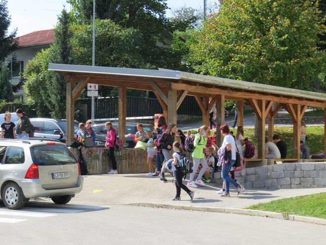 Pod nadstreškom učenke in učenci čakajo na šolski avtobus. FOTO: Bojan Rajšek/Delo