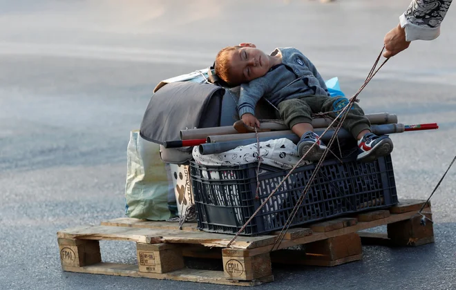 Begunka vleče otroka na paleti med selitvijo v novo začasno taborišče za migrante in begunce na otoku Lesbos v Grčiji. FOTO: Yara Nardi/Reuters