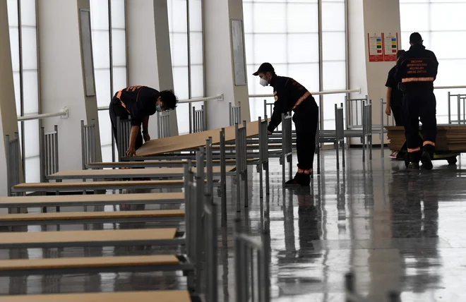 Pripadniki civilne zaščite med pripravo postelj v zagrebški športni areni, kjer naj bi, če bi bilo potrebno, namestili bolnike z blažjo ali srednje težko klinično sliko. FOTO: Denis Lovrovic/Afp