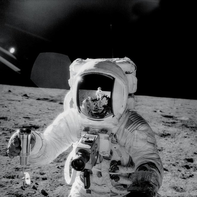 Astronavt Alan Bean med pobiranjem vzorca na Luni 20. novembra 1969. Na Zapestju leve roke je videti majhno knjižico z navodili. Odsev Peta Conrada je viden v vizirju čelade. FOTO: Nasa