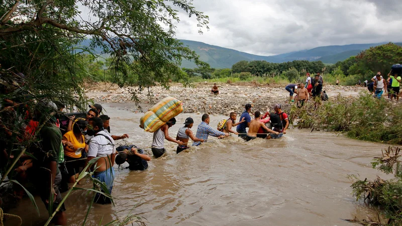 Fotografija: Na stotine Venezuelcev ki je obtičalo v Kolumbiji, je kljub visokem vodostaju poskušalo prečkati reko Tachira, ki je naravna meja med Kolumbijo in Venezuelo, da bi se vrnili v svojo domovino. FOTO: Schneyder Mendoza/Afp