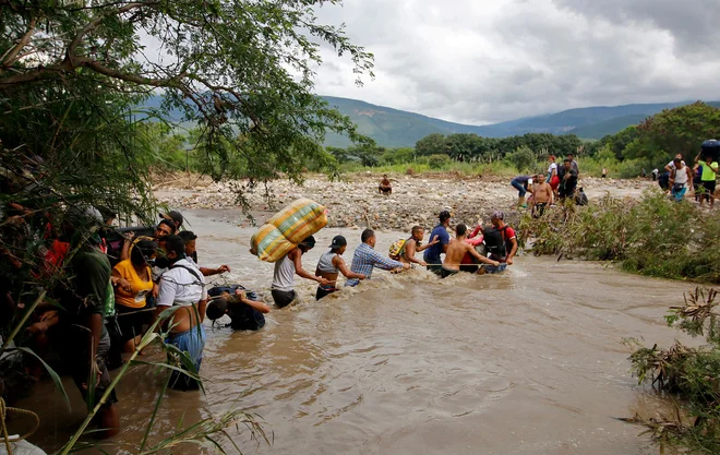 Na stotine Venezuelcev ki je obtičalo v Kolumbiji, je kljub visokem vodostaju poskušalo prečkati reko Tachira, ki je naravna meja med Kolumbijo in Venezuelo, da bi se vrnili v svojo domovino. FOTO: Schneyder Mendoza/Afp