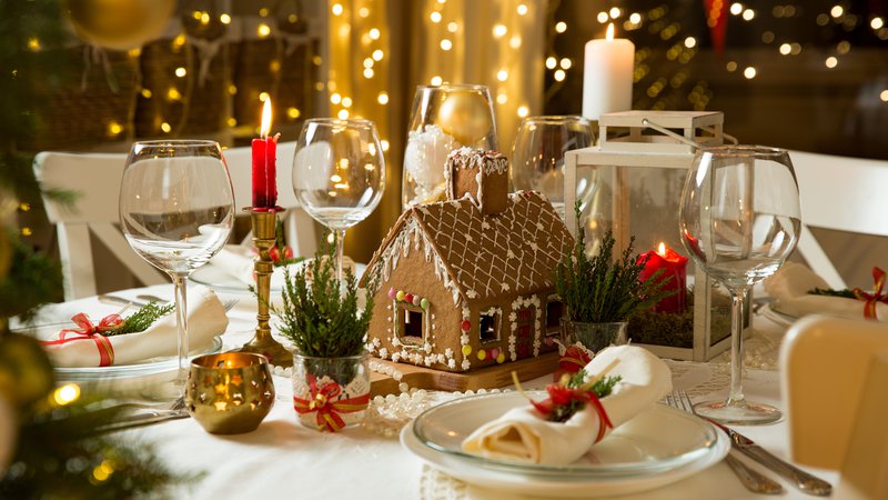 Fotografija: Medena hiška sredi belo pogrnjene mi­ze z zeleno-rdečimi dodatki bo skupaj s toplimi lučkami in prižganimi svečami ustvarila popolno božično-novoletno vzdušje. FOTO: Shutterstock