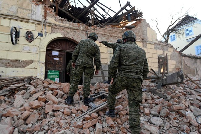 Hrvaški vojaki hodijo po razbitinah ob poškodovanih stavbah v Petrinji. FOTO: Denis Lovrovic/AFP