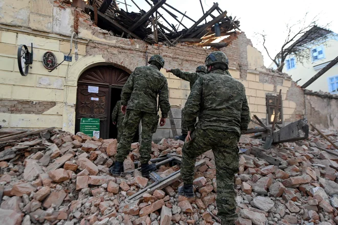 Hrvaški vojaki hodijo po razbitinah ob poškodovanih stavbah v Petrinji. FOTO: Denis Lovrovic/AFP