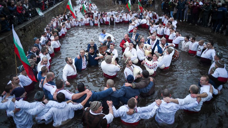 Fotografija: Bolgarski moški izvajajo tradicionalni ples horo v ledenih zimskih vodah reke Tundža v mestu Kalofer med praznovanjem pravoslavnega božiča, kljub omejitvam zaradi pandemije. Pravoslavni duhovnik vrže križ v reko, tisti, ki ga bo ujel prvi, naj bi ostal zdrav skozi vse leto, pa tudi vsi, ki plešejo v ledenih vodah. FOTO: Nikolay Doychinov/Afp