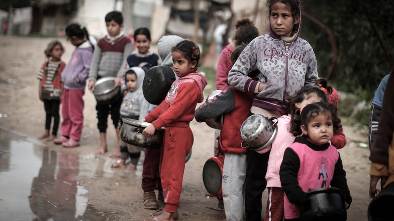 Fotografija: V revni soseski Gaze otroci v rokah držijo lončke, ko čakajo na obrok hrane, pripravljen iz sestavin, pridobljenih od donatorjev, ki želijo pomagati pomoči potrebnim družinam. FOTO: Mahmud Hams/Afp