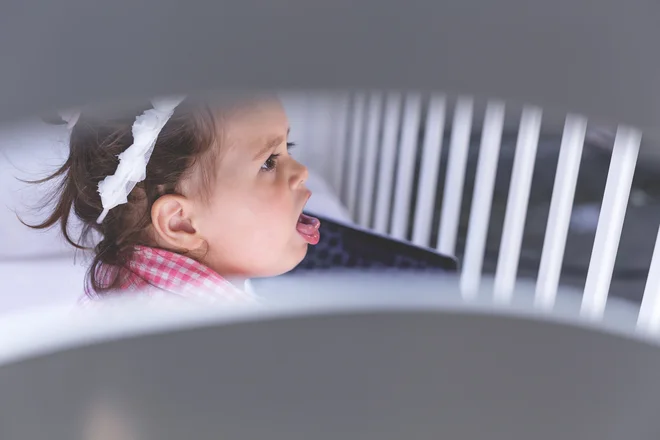 one year old baby is coughing while sitting in a crib beside a laptop in a plaid shirt