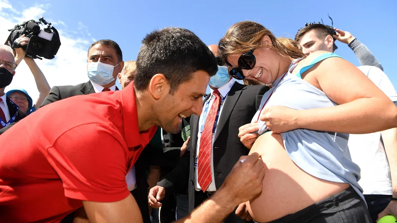 Fotografija: Po finalni zmagi je moral Novak Đoković podeliti številne avtograme navijačem: enega tudi skorajšnji mamici na nenavadno mesto. FOTO: William West/AFP