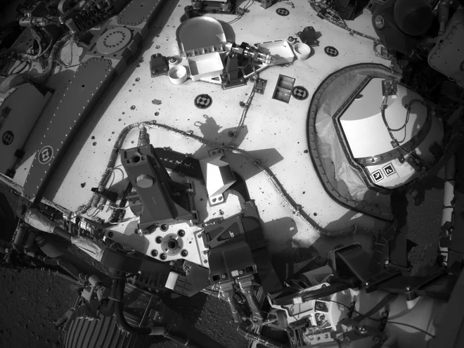 Posnetek roverja s kamero Navcam na roverju. Na fotografiji je videti ploščica z upodobitvijo preteklih roverjev na Marsu in helikopterčka. FOTO: NASA/JPL-Caltech