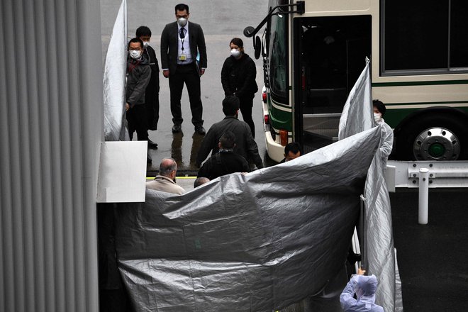Japonski uradniki držijo plastične prevleke med vstopanjem skupine potnikov v avtobus iz letala, o katerem se domneva, da je prevažal obtožena očeta in sina Taylor. FOTO: Kazuhiro Nogi/AFP