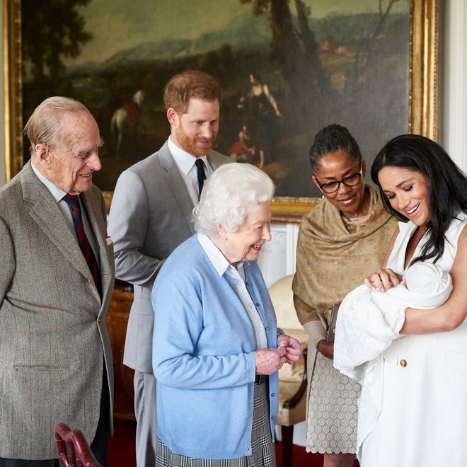 Kraljica, princ Philip, Harry, Meghan in njena mati, Doria Ragland, občudujejo malega Archieja. Ta bo kmalu dobil sestrico, očitno pa se bo nekdo v kraljevi družini spet spraševal, kako »temna« bo deklica. FOTO: Chris Allerton/Reuters
