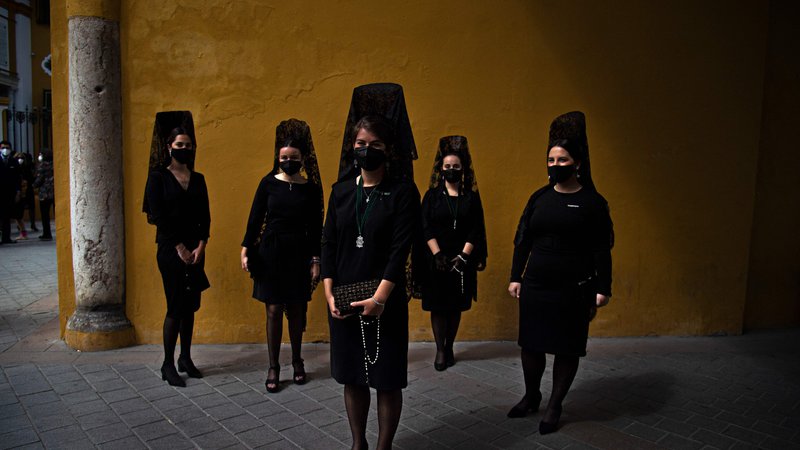 Fotografija: Ženske oblečene v črnino stojijo na ulici v Sevilli, kljub temu, da je že drugo leto zapored zaradi koronavirusa odpovedana verska procesija ob Svetem tednu. FOTO: Cristina Quicler/Afp