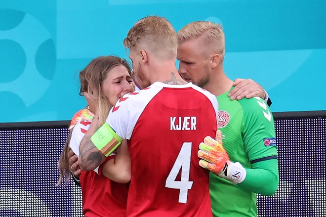 Danski vratar Kasper Schmeichel in kapetan Simon Kjær ob robu igrišča tolažita hudo zaskrljeno Eriksenovo partnerico Sabrino Kvist Jensen. FOTO: Wolfgang Rattay/AFP