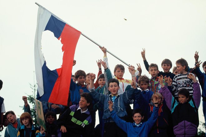 Otroci s slovensko zastavo z izrezano peterokrako zvezdo pri vojašnici JLA Slave Klavora v Mariboru 23. maja 1991, ko je Jugoslovanska ljudska armada obkolila učni center Teritorialne obrambe v Pekrah. FOTO: Joco Žnidaršič