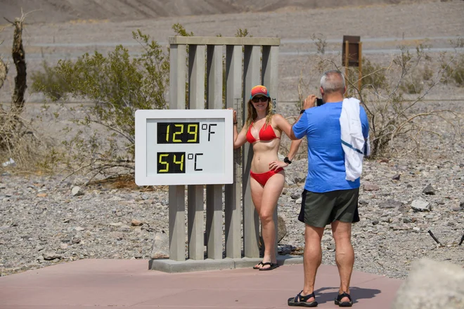 John Gillette fotografira Sarah Null v kopalkah poleg termometra, ki kaže 54 stopinj Celzija v centru za obiskovalce v narodnem parku Death Valley v Kaliforniji. Velik del zahoda ZDA je ta teden pripravljen na rekordne vročinske valove. FOTO: Patrick T. Fallon/Afp