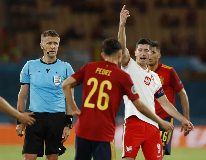 Robert Lewandowski ob sodniku Danieleju Orsatu med tekmo v Sevilli. FOTO: Marcelo Del Pozo/Reuters