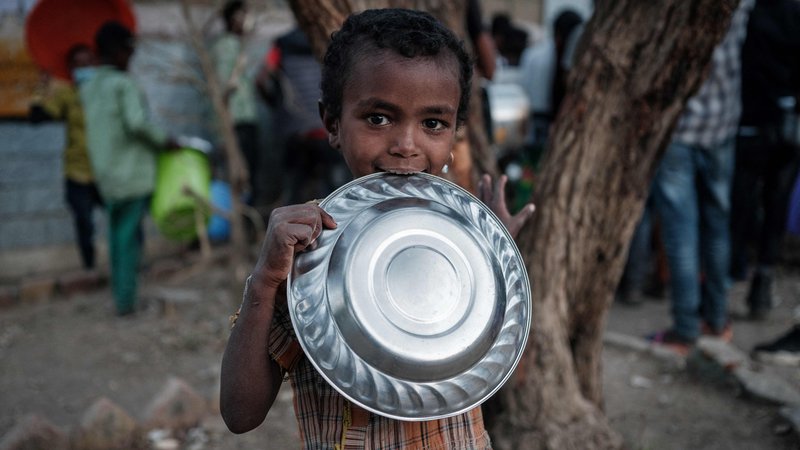 Fotografija: Otrok, ki je pobegnil pred nasiljem iz etiopske regije Tigray, pred osnovno šolo May Weyni čaka na večerjo, saj le ta predstavlja edini dnevni obrok. OŠ se je spremenila v taborišče za notranje razseljene osebe. FOTO: Yasuyoshi Chiba/Afp