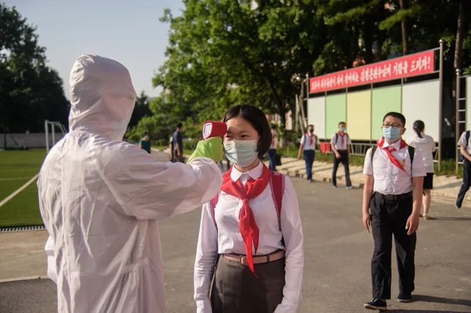 Učenki pred vstopom v srednjo šolo v Pjongjangu merijo temperaturo. FOTO: Kim Won Jin/AFP