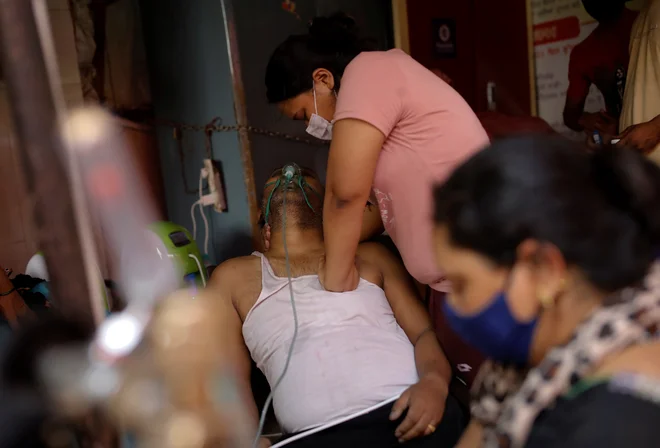 V indijskem mestu Ghaziabad Manisha Bashu masira prsi svojega očeta, ki ima težave z dihanjem, potem ko je izgubil zavest kljub dodatnem kisiku. FOTO: Adnan Abidi/Reuters<br />
