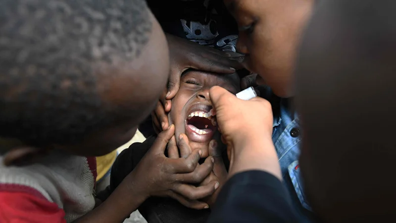 Fotografija: Na ulici v Nairobiju zdravstveni delavec daje otroku zdravilo proti otroški paralizi. Ta bolezen je zelo nevarna in lahko povzroči paralizo in vseživljenjsko invalidnost. Potem ko je bilo potrjeno, da virus kroži, so se kenijska vlada, UNICEF, WHO in partnerji odločili za cepljenje treh milijonov otrok v 13 okrožjih Kenije. FOTO: Simon Maina/Afp