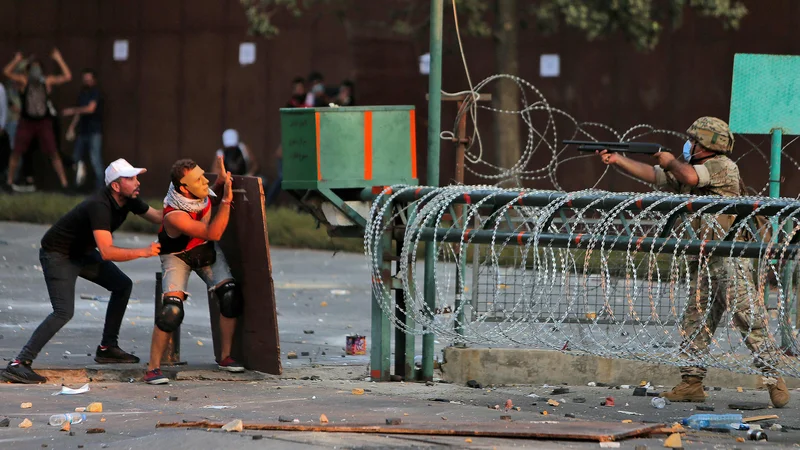 Fotografija: Ob prvi obletnici silovite eksplozije (214 mrtvih, okoli 6000 ranjenih), ki je razdejala mesto, so le streljaj stran od glavne spominske slovesnosti, posvečene eksploziji v bejrutskem pristanišču, potekali množični protesti. Protestniki so zažigali gume in skušali vdreti v stavbo parlamenta, ker da poslanci zavlačujejo z izsledki preiskave tragedije. FOTO: Afp