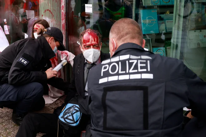Aktivist okoljskega gibanja Extinction Rebellion, prekrit z barvo in z rokami prilepljenimi na okna stranke Konrad-Adenauer-Haus, sedeža stranke Krščansko demokratske unija (CDU) v Berlinu, gleda policista, ki skuša odstraniti protestnike. FOTO: Odd Andersen/Afp<br />
