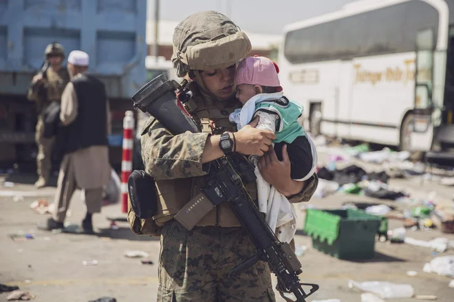 Članica 24. pomorske ekspedicijske enote (MEU) ameriške mornarice nosi otroka skozi center za nadzor evakuacije (ECC) na mednarodnem letališču Hamid Karzai v Kabulu, na zadnji dan pred dokončnim umikom ameriške vojske iz Afganistana. FOTO: Afp<br />
