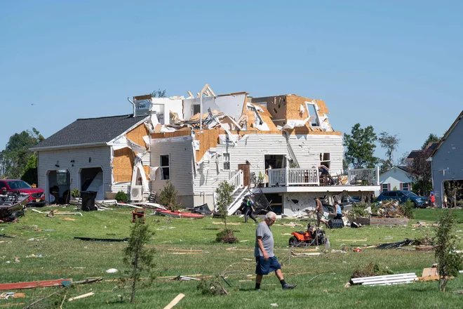 Moški se sprehaja ob hiši v New Jerseyju, ki jo je poškodoval tornado, potem ko je območje preplavilo rekordno število padavin, ki so jih prinesli ostanki orkana Ida. FOTO: Branden Eastwood/Afp<br />
