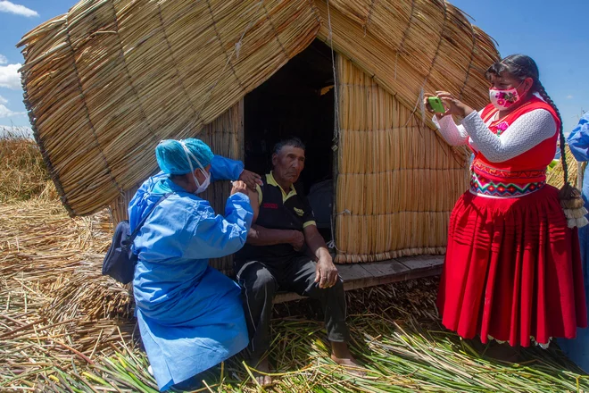 Delavec perujskega ministrstva za zdravje cepi lokalnega prebivalca v okviru programa za imunizacijo ranljivega prebivalstva na plavajočem otoku Uros na jezeru Titicaca, v Peruju. Več kot 1700 članov domorodnega ljudstva Uros živi na približno 140 umetno narejenih plavajočih otokih iz trsja. FOTO: Carlos Mamani/Afp<br />
<br />
