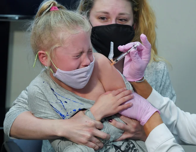 V ameriškem mestu Storrs je 7-letna Emma Ingle, ki sedi v naročju svoje matere Kim Obert, prejela svoj prvi odmerek Pfizer cepiva proti koronavirusu. FOTO: Michelle Mcloughlin/Reuters
