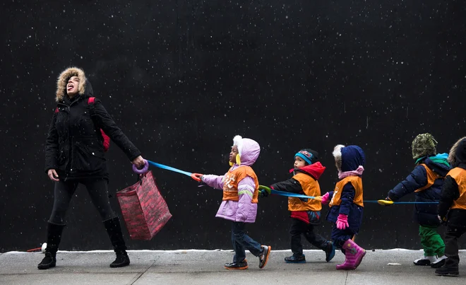 Učiteljica skuša z usti ujeti snežinke, medtem ko pelje iz šole svoje učence v knjižnico v newyorški soseski Harlem, ki se nahaja v okrožju Manhattan. FOTO: naslavlja Latif/Reuters

