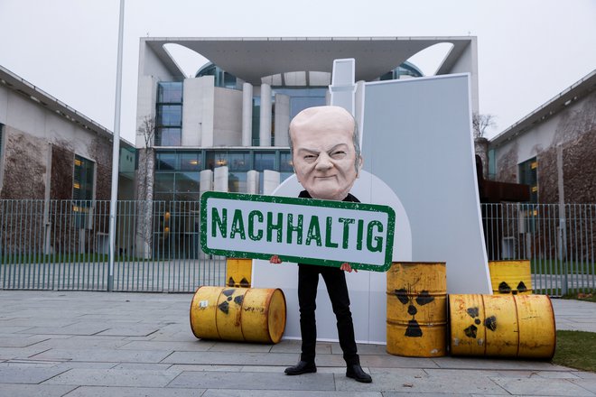 Protestnik z masko, ki predstavlja kanclerja Olafa Scholza, drži plakat z napisom "Trajnost", medtem protestom proti 'zelenjenju' jedrske energije. FOTO: Michele Tantussi/Reuters
