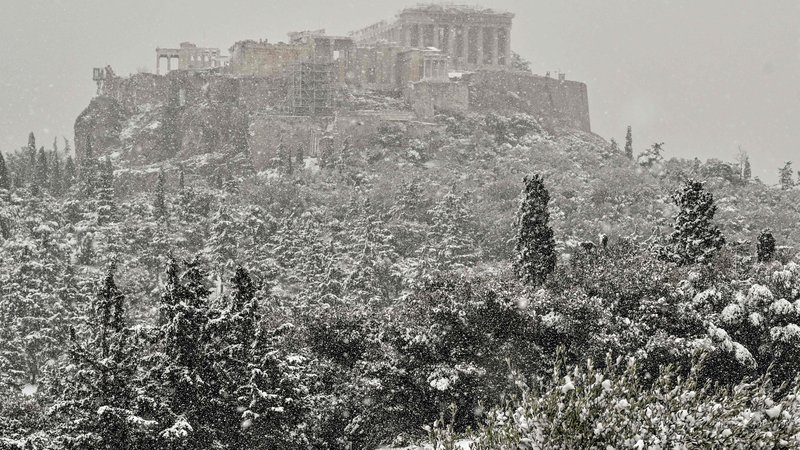 Fotografija: Redek pogled na povsem zasneženo Akropolo, pod katero sneg povzroča tudi vrsto preglavic. Na območju Aten zelo redko sneži. FOTO: Louisa Gouliamaki/AFP
