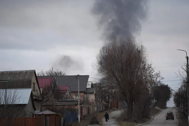 Lokalni prebivalec hodi po ulici, v ozadju pa dim, ki se dviga v bližini mesta Hostomel in letališča Antonov na severozahodu Kijeva. FOTO: Daniel Leal/AFP