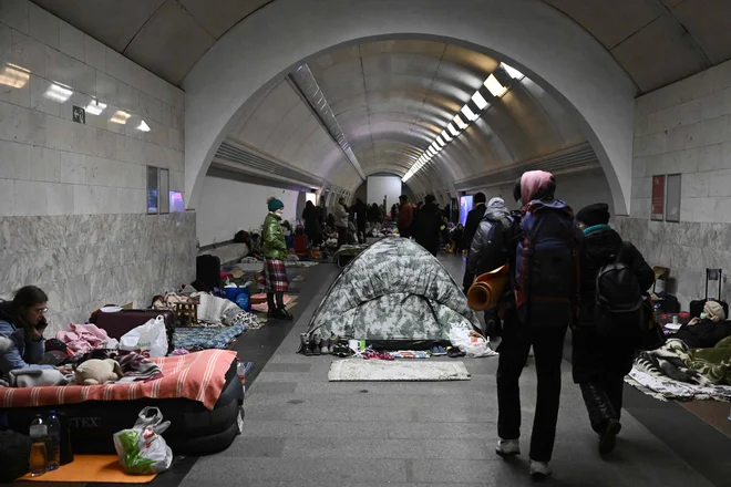 Civilisti hodijo mimo prebivalcev Ukrajine, ki uporabljajo podzemno postajo podzemne železnice kot zaklonišče pred bombnimi napadi. FOTO: Aris Messinis/AFP