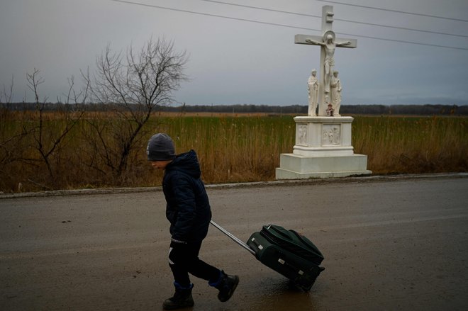 Fant, ki beži pred konfliktom v Ukrajini, hodi s kovčkom mimo razpela, potem ko je prečkal mejo med Moldavijo in Ukrajino v bližini mesta Palanca. FOTO: Nikolay Doychinov/AFP
