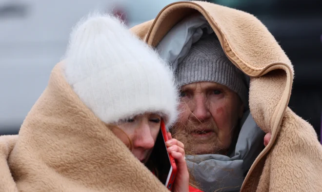 Ženski se poskušata zaščititi z odejami v centru za begunce, vzpostavljenem v nekdanjem trgovskem centru v poljskem Przemyslu. FOTO: Fabrizio Bensch/Reuters