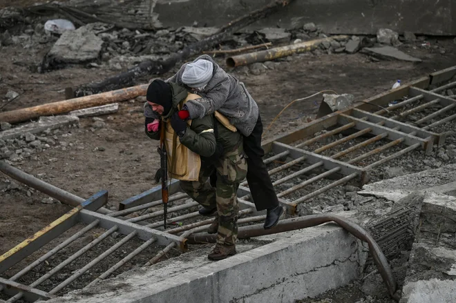 Vojak nosi žensko na hrbtu na begu iz Irpina. FOTO: Aris Messinis/AFP