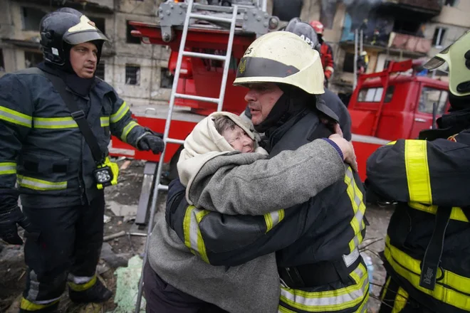 Starejša ženska objema gasilca, potem ko so jo evakuirali iz stanovanjske hiše v Kijevu, uničene v ruskem zračnem napadu. Foto: Afp
