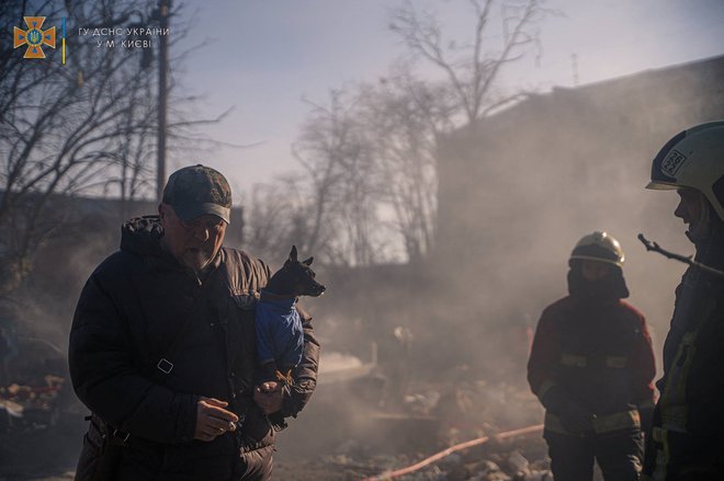 Moški s psom med evakucijo iz uničene stavbe v Kijevu. FOTO: State Emergency Service/Reuters
