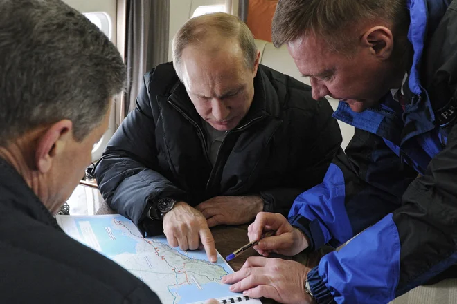 Predsednik Vladimir Putin v helikopterju, obdan s sodelavci in zemljevidi, leta 2016 nad obalo Krima. FOTO: Mihail Klimentjev/AFP
