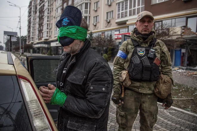 Policist straži zajetega plenilca v mestu Irpin, medtem ko se ruski napad na Ukrajino še kar nadaljuje. FOTO:&nbsp;Oleksander Ratušnjak/Reuters
