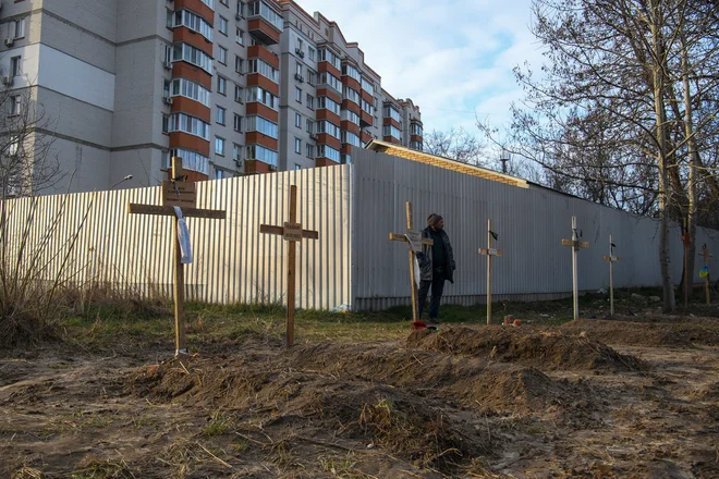 Moški stoji ob grobovih s trupli civilistov, ki so jih po navedbah lokalnih prebivalcev ubili ruski vojaki v Buči. FOTO: Stringer/Reuters
