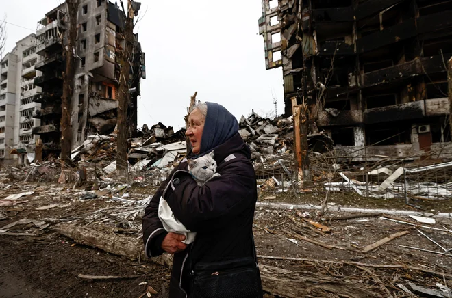 Ženska nosi svojo mačko mimo zgradb, ki so bile uničene zaradi ruskega obstreljevanja za granatami med rusko invazijo na Ukrajino v Borodjanki. FOTO Zohra Bensemra/Reuters
