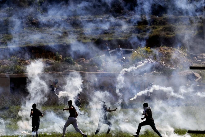 Palestinci se skrivajo pred solzivcem med spopadi z izraelskimi varnostnimi silami na severnem vhodu v Ramalo v bližini izraelske naselbine Beit El, na okupiranem Zahodnem bregu. Foto: Abbas Momani/Afp