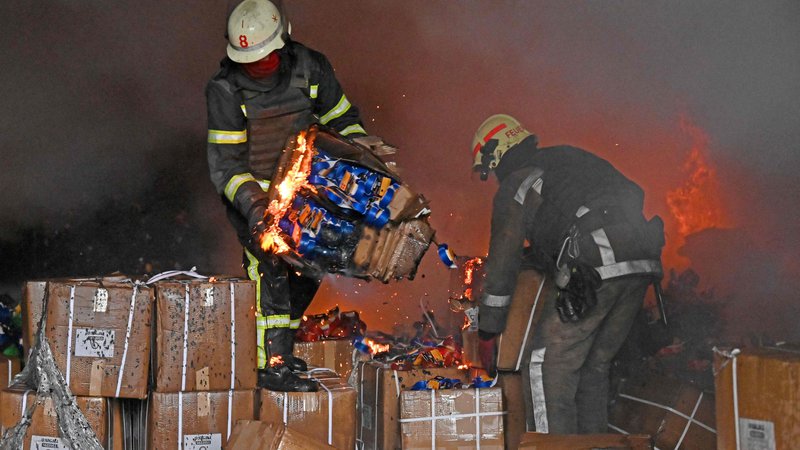 Fotografija: Gasilci rešujejo škatle, medtem ko skušajo pogasiti požar po tem, ko je raketa zadela skladišče na obrobju Harkova. Foto: Sergej Bobok/Afp
